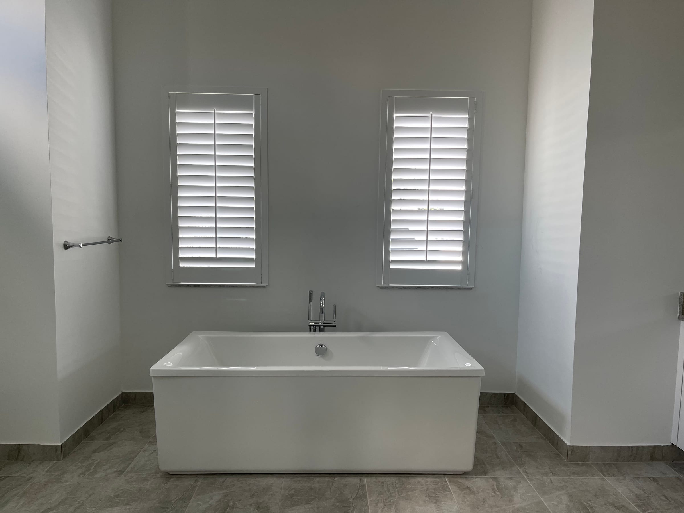 White shutters on two windows above a freestanding bath