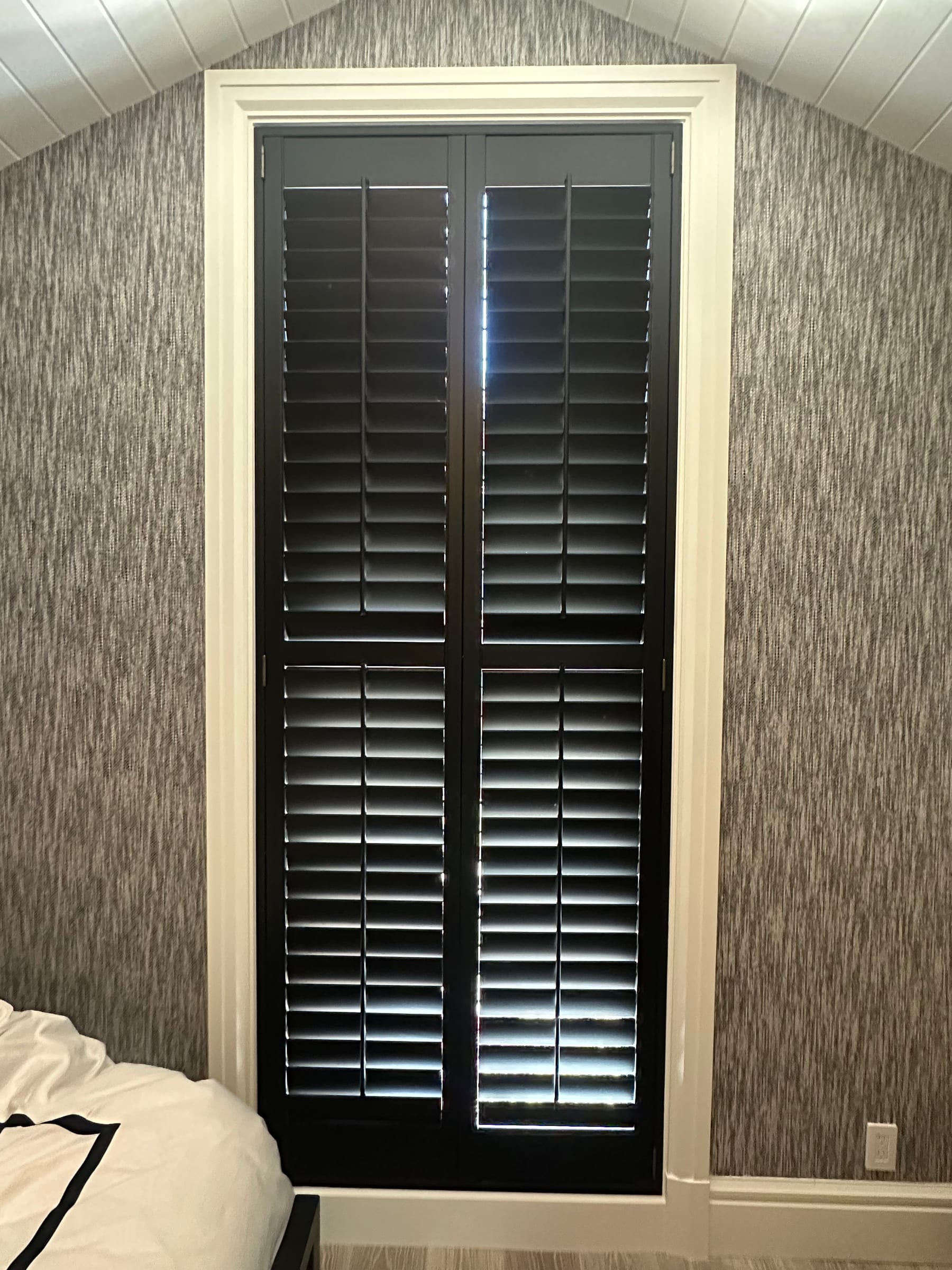 Black shutters framing a bedroom window against textured wallpaper