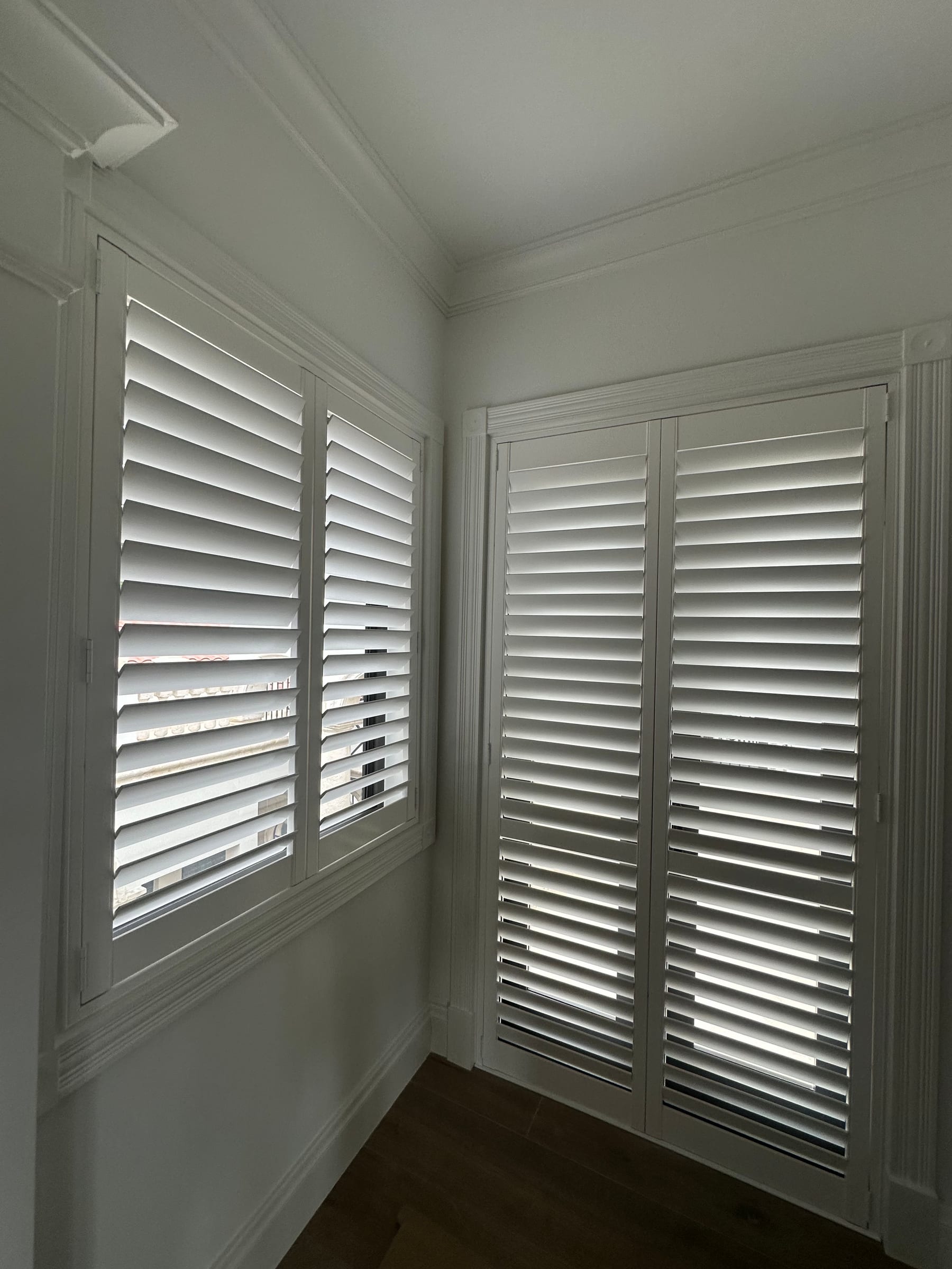 Two tall white shutter panels meeting at a corner beside a doorway