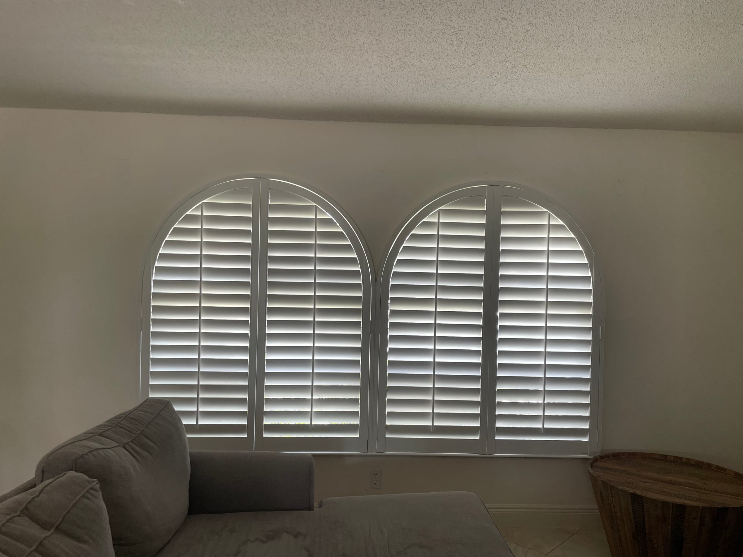 White shutters in two arched windows above a sofa