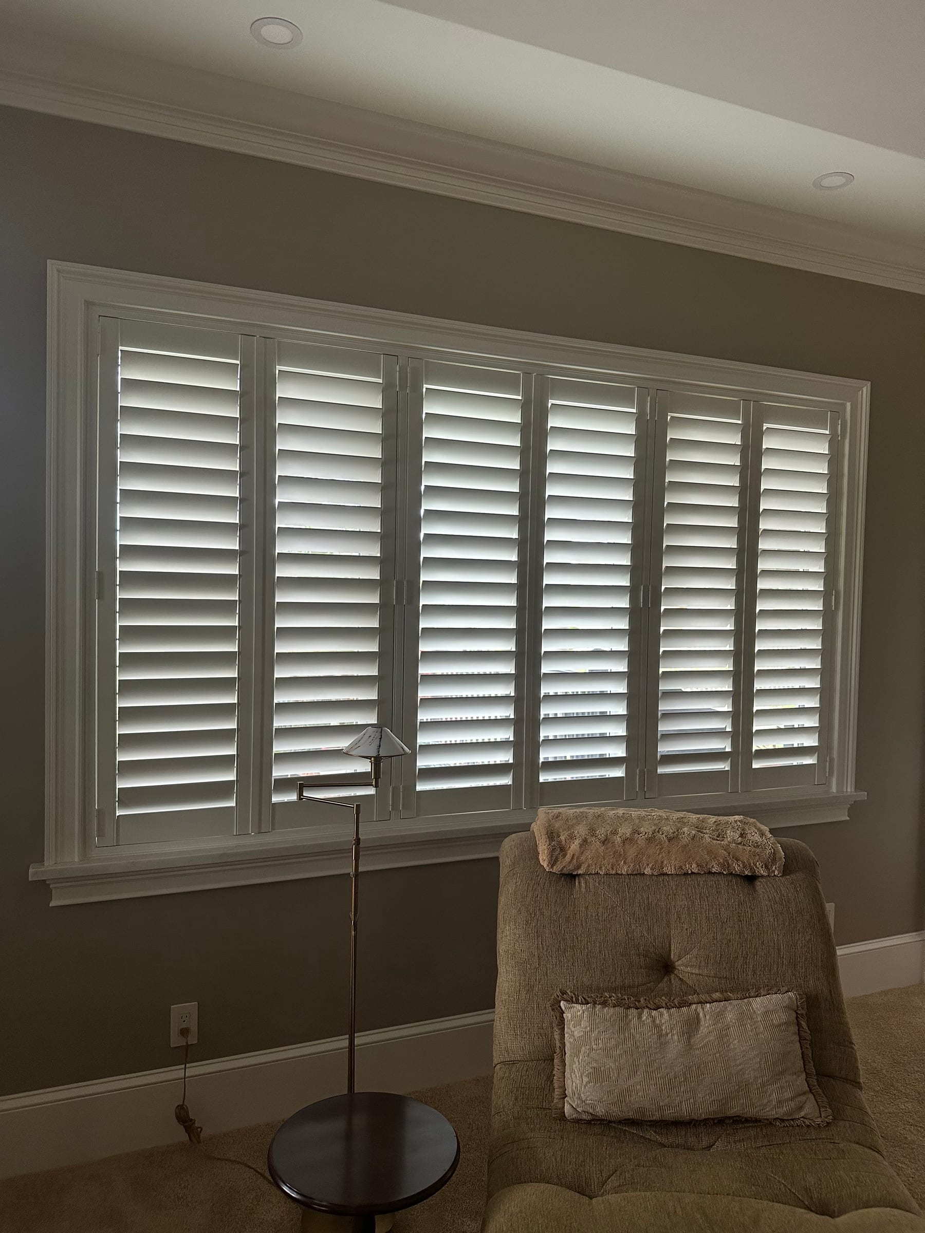 White shutter panels spanning a wide living-room window, louvers angled open
