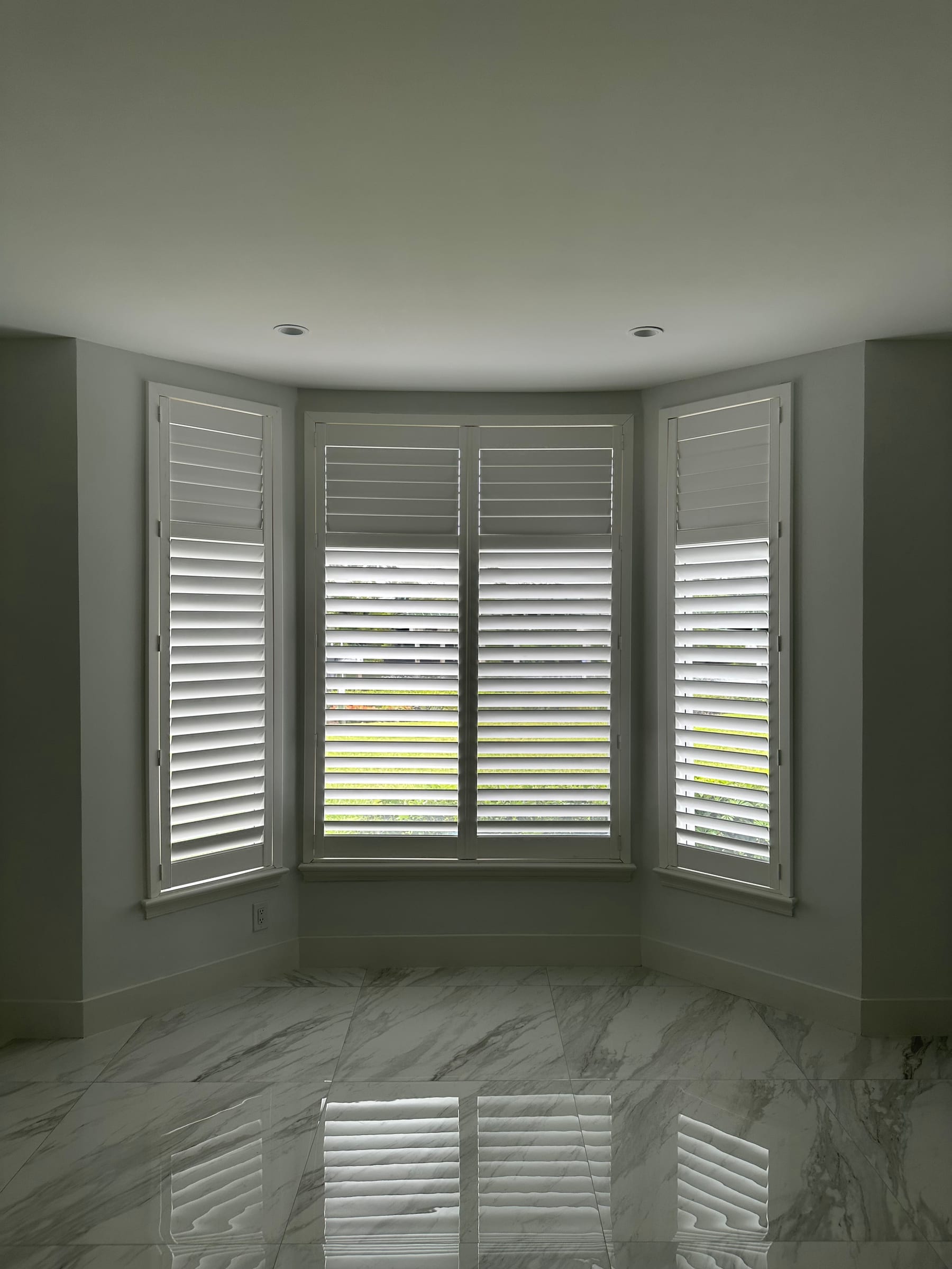 White shutters following a three-sided bay window in a green-walled room