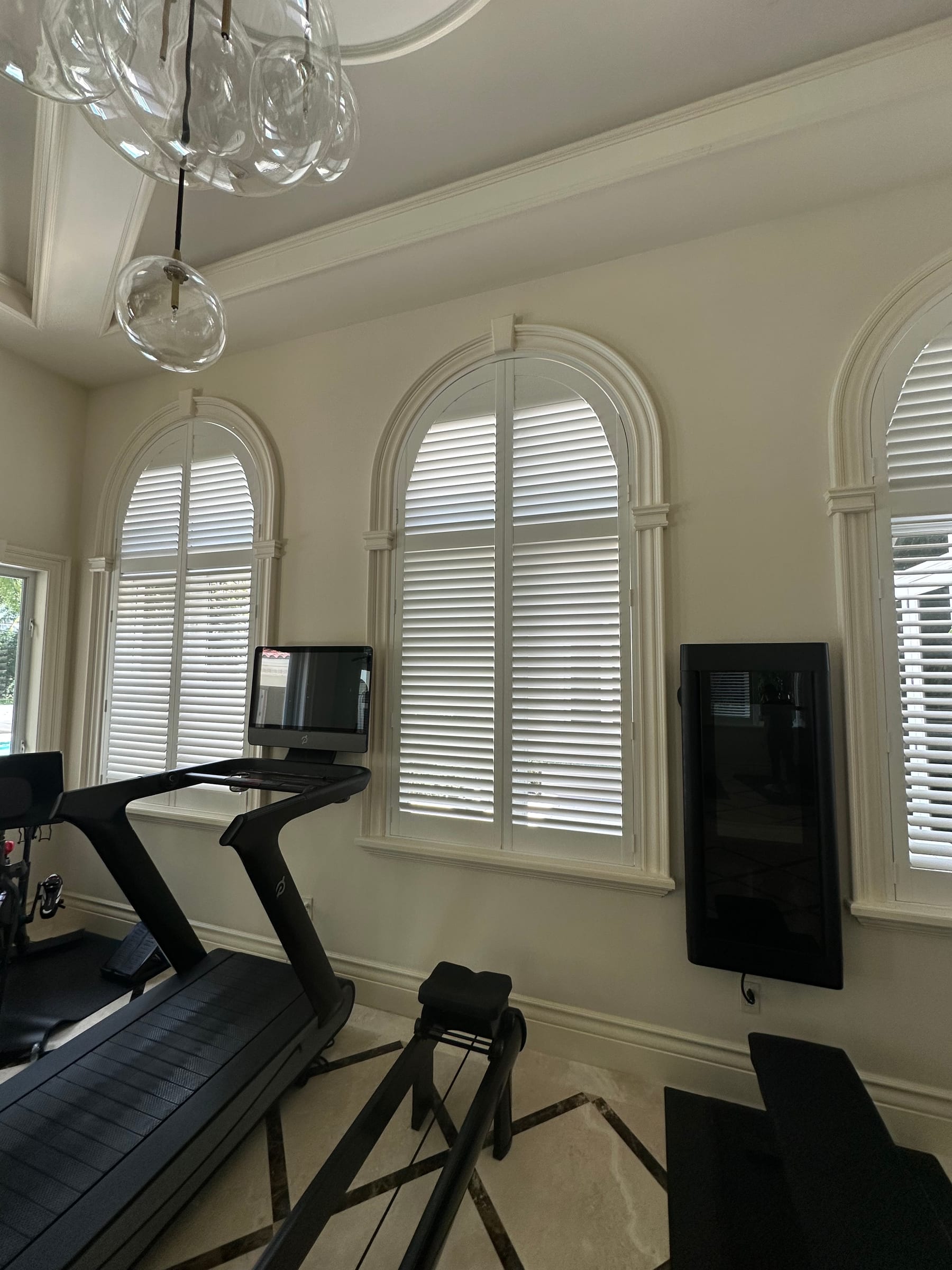 White shutters in arched windows above exercise equipment