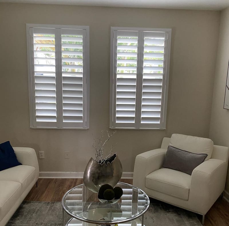 White shutters on two windows above a pale sofa and armchair