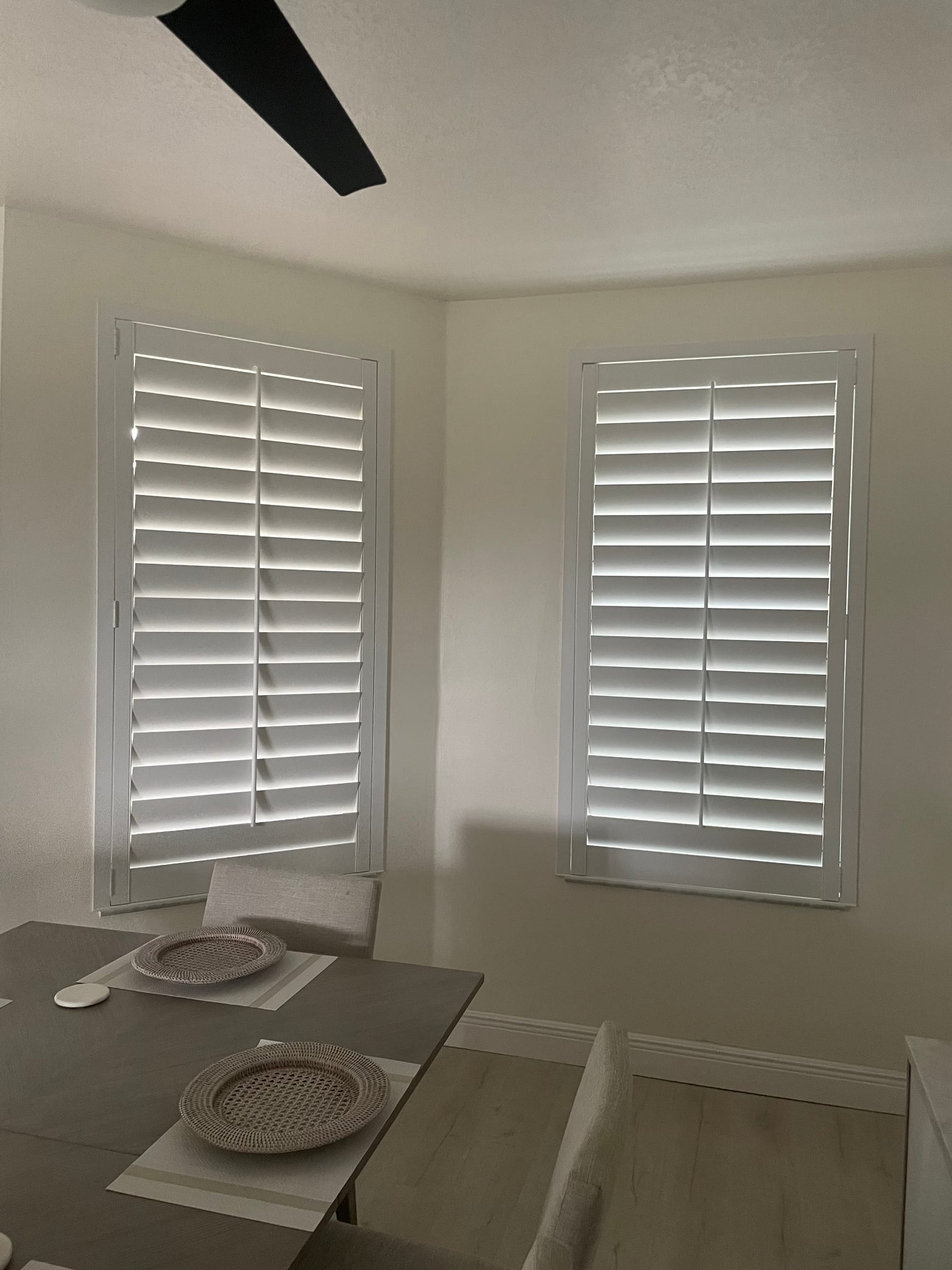 White shutters on two windows meeting at a corner above a dining table