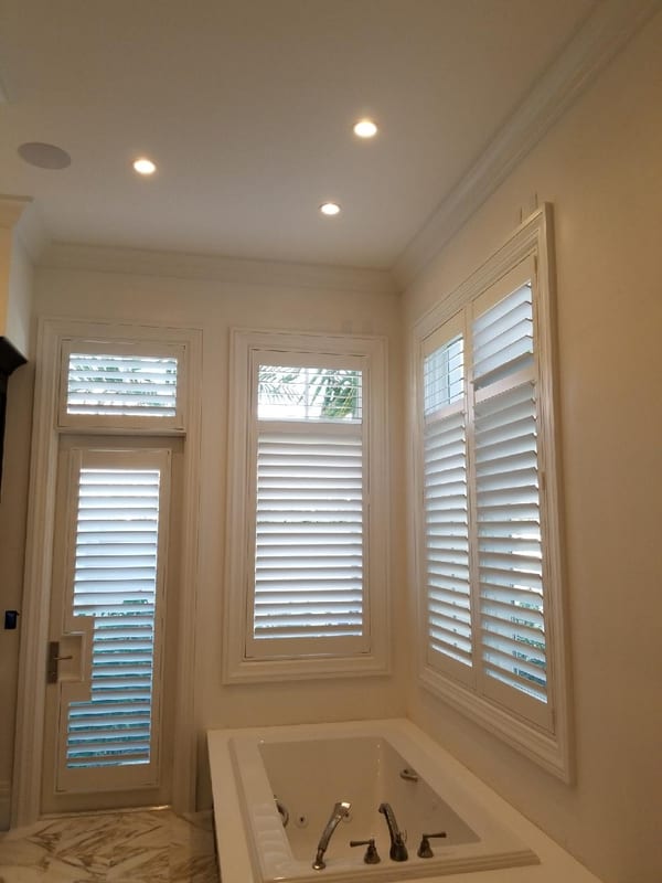 White shutters on a bathroom window and door beside a built-in bath