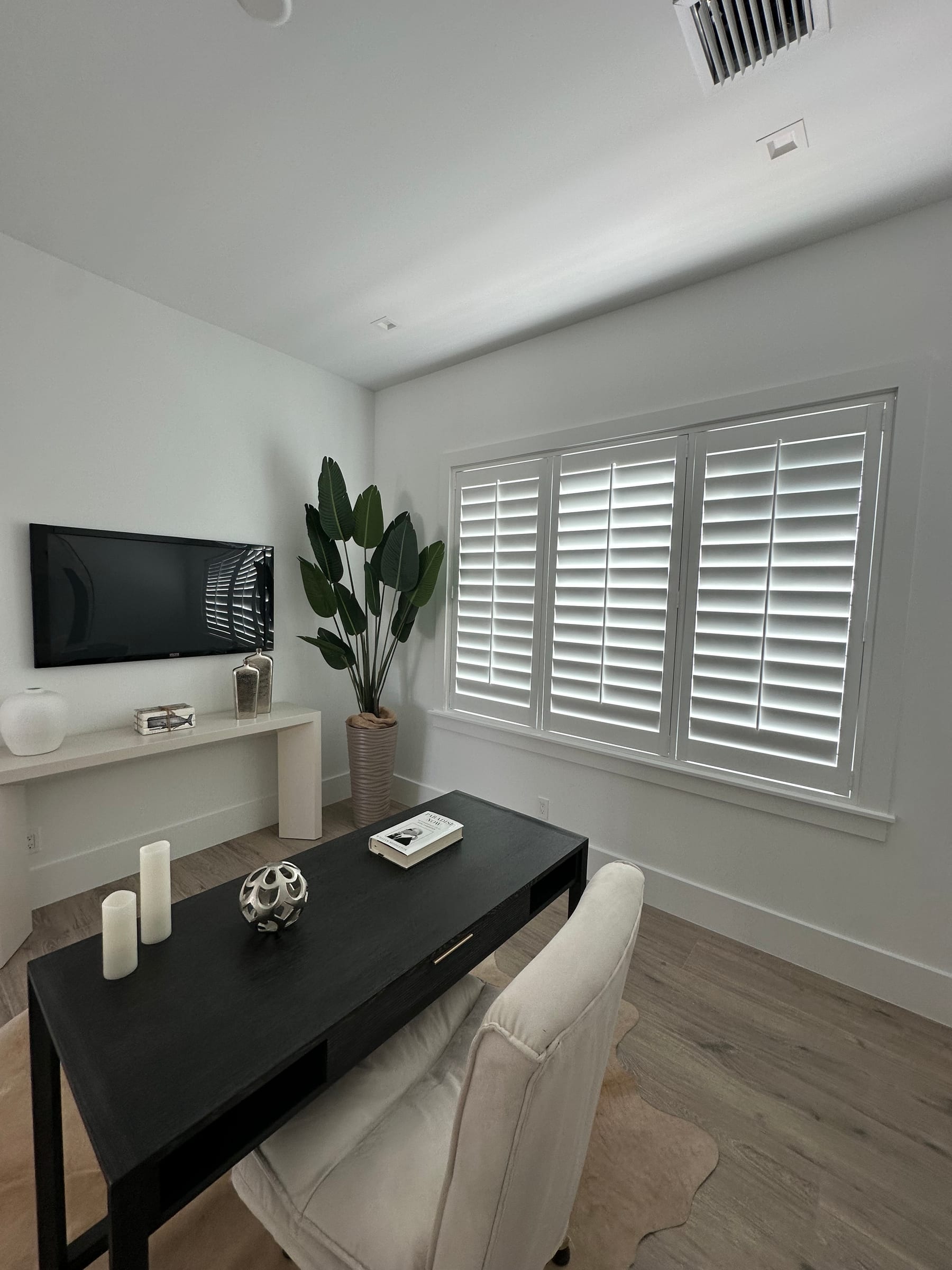 White shutters on a window beside a console table and a potted plant