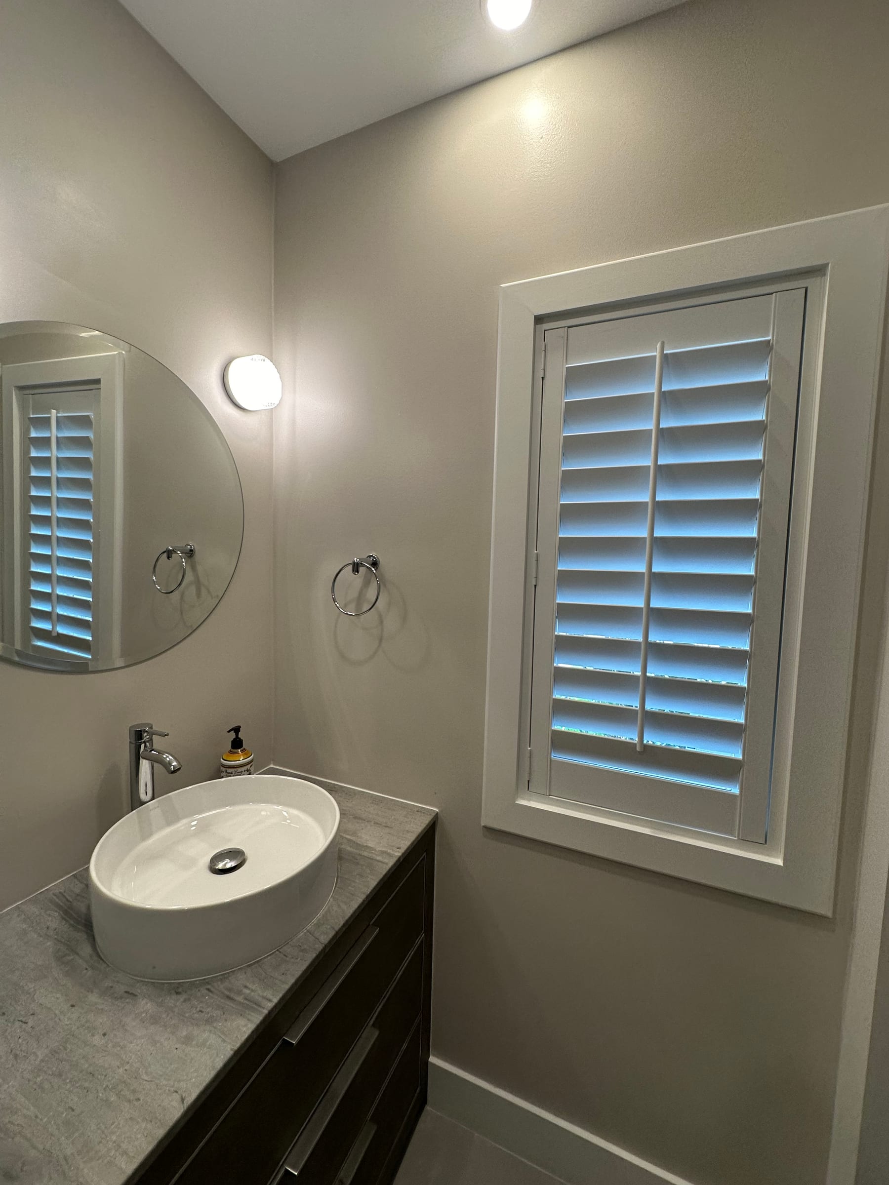 A narrow white shutter beside a vessel sink in a modern bathroom
