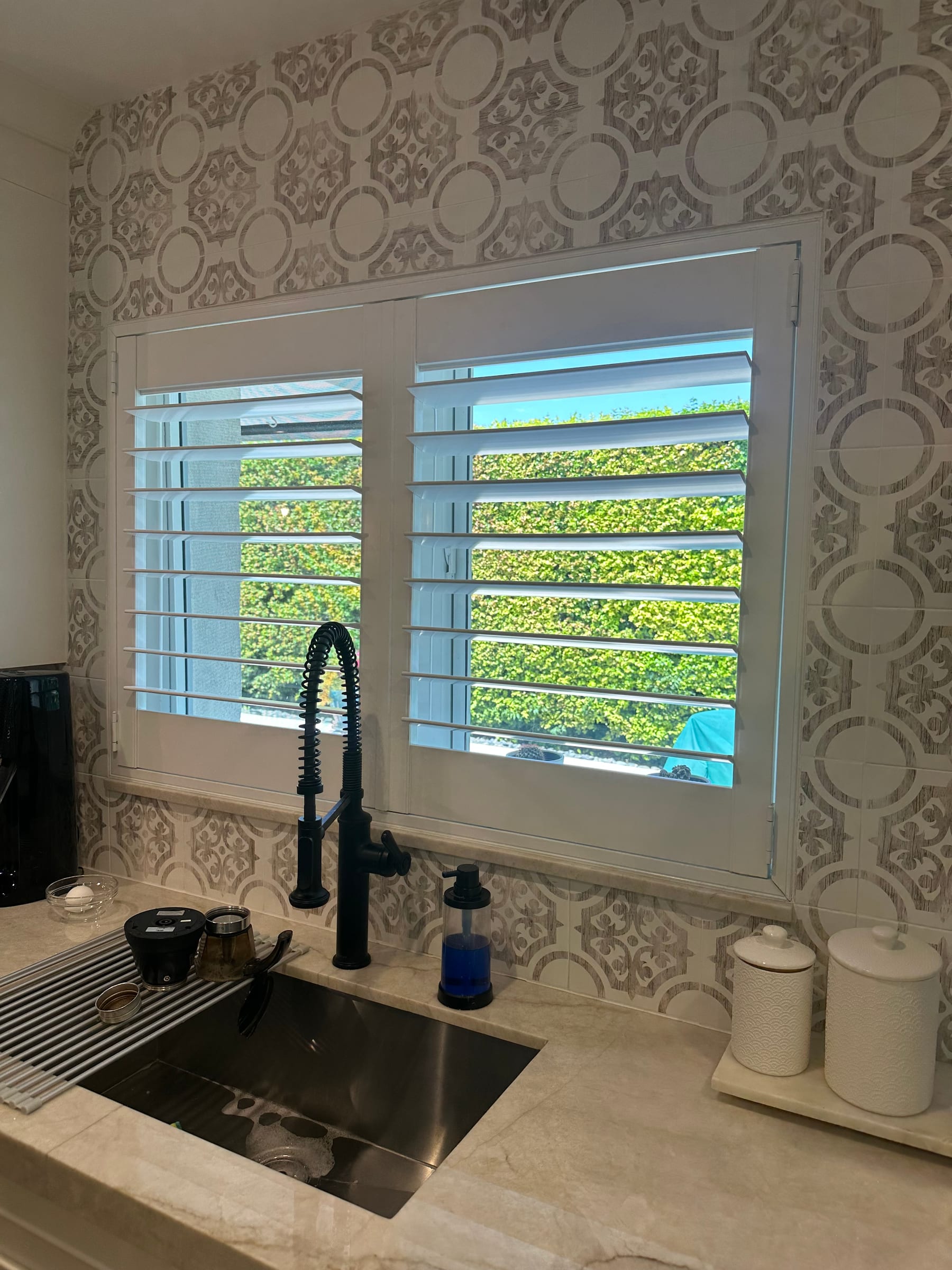 A white shutter above a kitchen sink against patterned tile