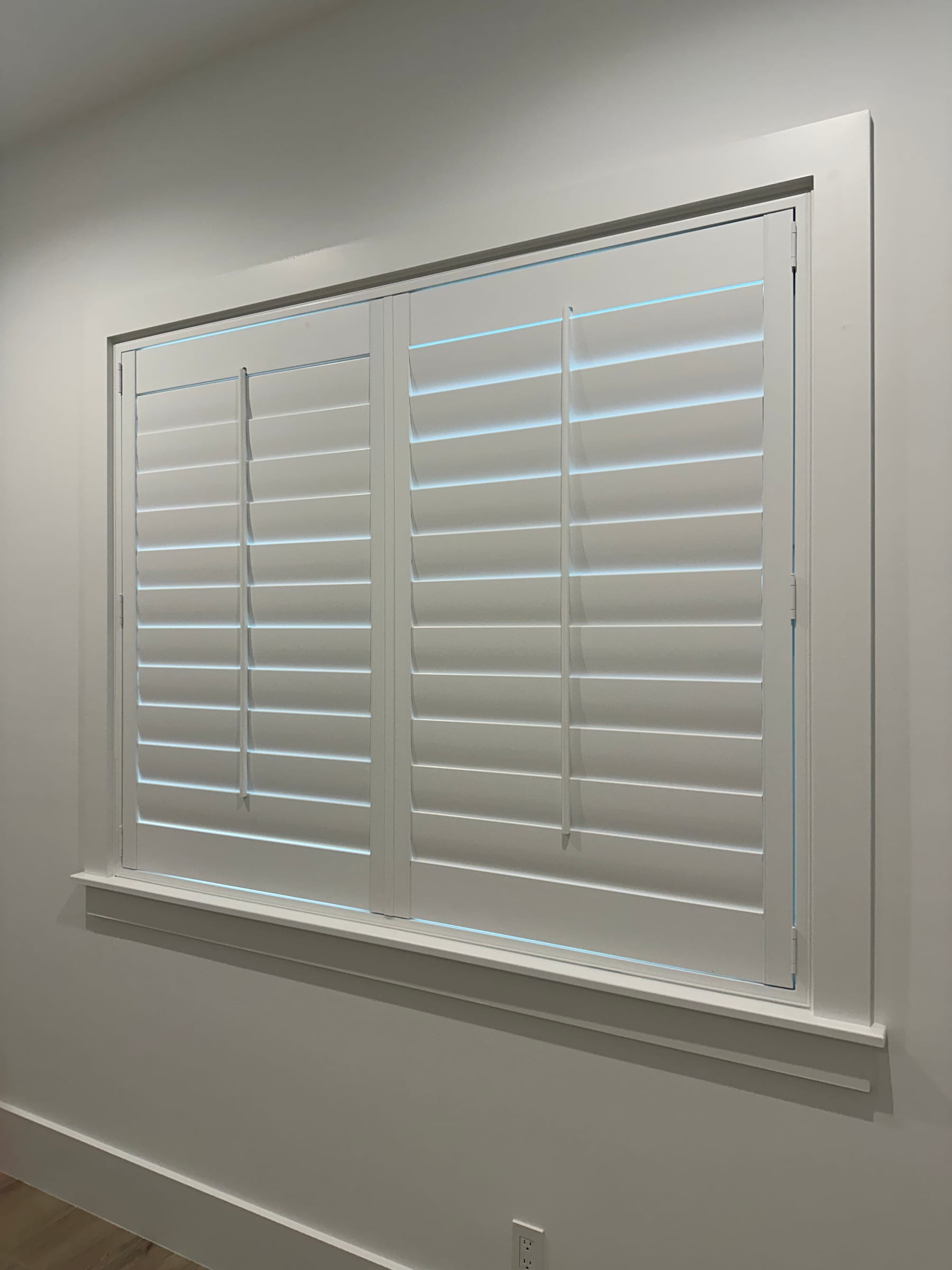A wide white shutter with a divider rail, louvers closed